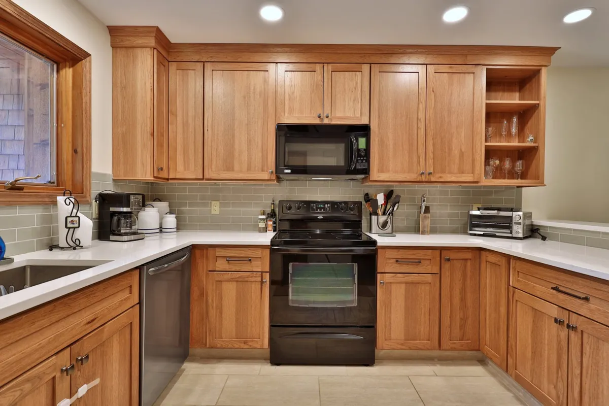 A welcoming kitchen with warm wood cabinetry, sleek black appliances, and bright white countertops. The space appears spacious and organized, with plenty of room for meal prep and cooking. The cabinetry and appliances suggest modern conveniences, such as a dishwasher and coffee maker, while the inviting mood hints at family gatherings and shared moments.