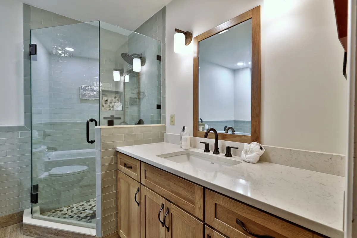 A newly renovated bathroom featuring a spacious glass shower enclosure, a double sink vanity with wooden cabinetry, large mirrors, and modern fixtures. The bathroom exudes a tranquil and luxurious atmosphere, ideal for relaxation and self-care.