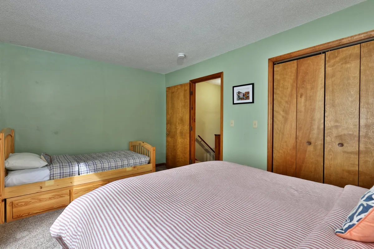 An inviting bedroom with both a bunk bed and a queen bed, wooden closet doors, and a framed picture on the wall. The room suggests flexibility for families or groups, providing multiple sleeping arrangements in a warm, relaxed setting.