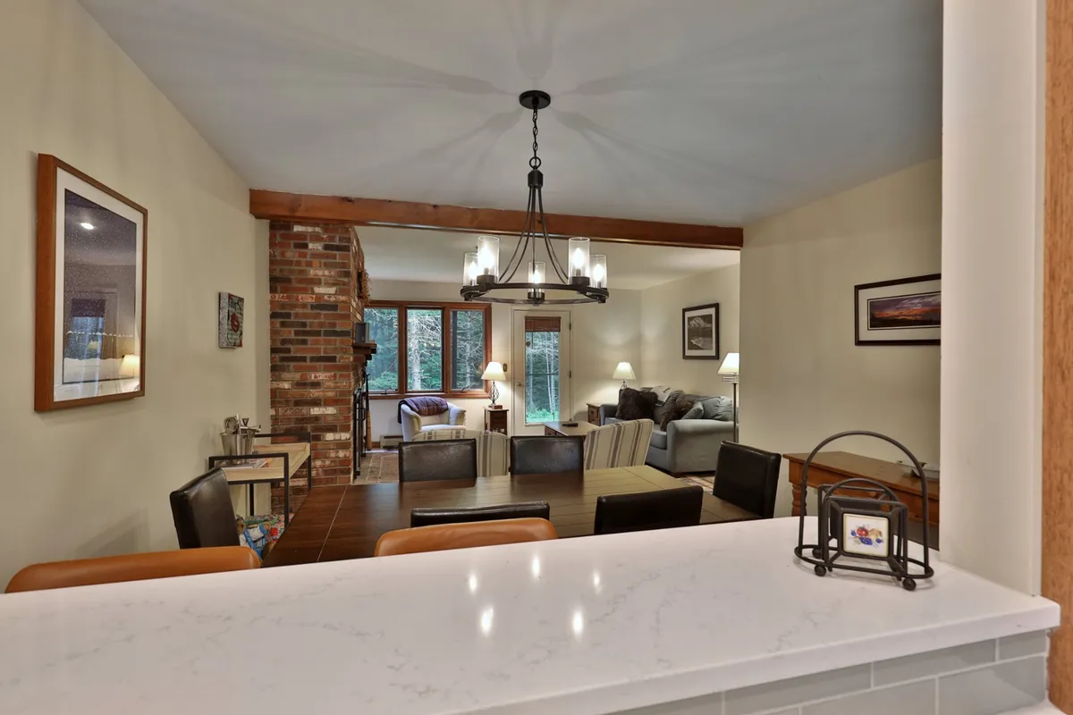 A warm, inviting interior scene featuring a dining table and a living area with large windows letting in natural light. The brick wall and cozy furnishings create a welcoming atmosphere for family dinners or relaxing after a day outdoors.
