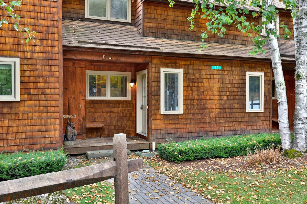 The exterior of the Glazebrook E2 condo with a welcoming wooden facade and a front porch surrounded by lush greenery. The porch is inviting, perfect for sipping coffee while watching the colors of autumn unfold. The house number is visible, grounding the home in its scenic setting.