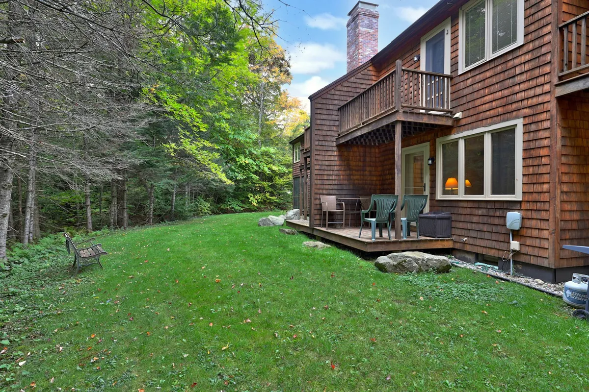 A spacious wooden deck overlooking a green lawn and surrounded by trees, with outdoor seating and plenty of room for group gatherings or relaxing after a day outdoors.