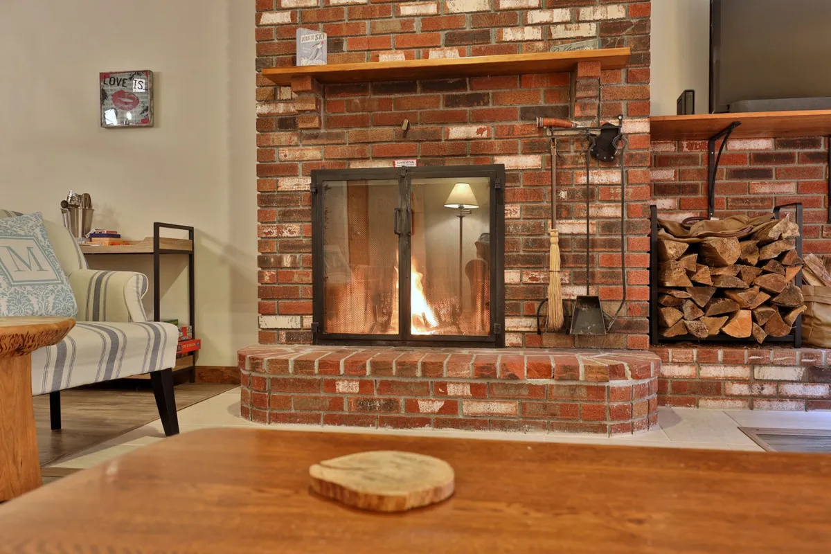 A cozy, inviting living area featuring a wood-burning fireplace, wooden shelves, a stack of firewood, and comfortable seating—ideal for warming up and relaxing with family or friends after a day outdoors.