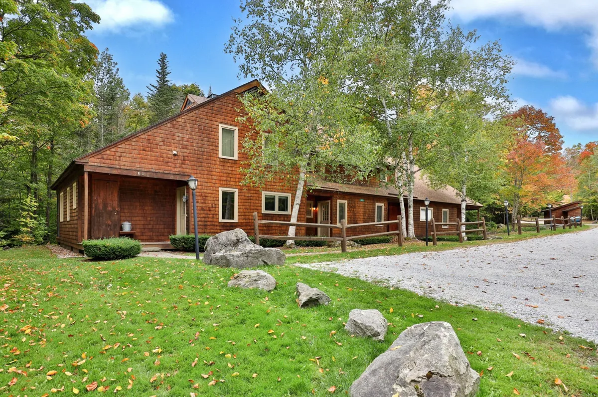 The exterior of the property is framed by lush greenery, a gravel driveway, and large boulders, creating a welcoming and nature-connected atmosphere perfect for family gatherings, outdoor barbecues, or starting an exploration of nearby trails.