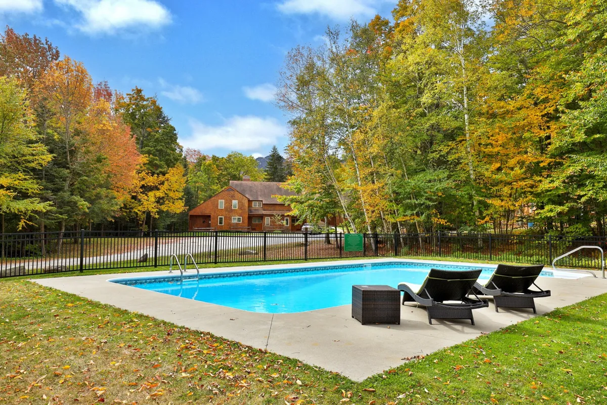 This image features a tranquil outdoor heated swimming pool surrounded by lounge chairs and lush trees, with the house visible in the background. The environment suggests a relaxed, resort-style atmosphere ideal for summer enjoyment.