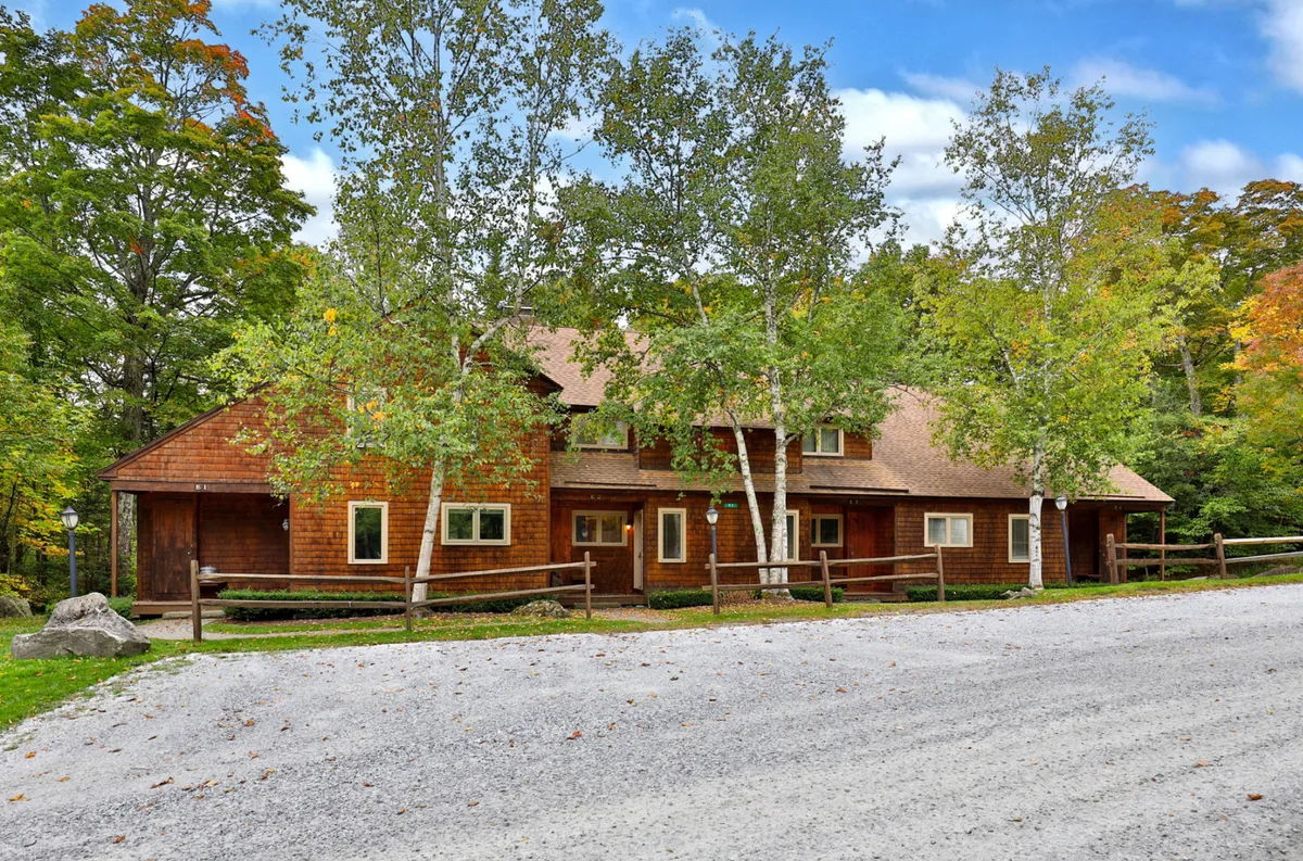 This image shows the wooden facade of Glazebrook E2, surrounded by trees and a gravel driveway, with a visible fence. The setting conveys a welcoming, tranquil environment with easy access to outdoor activities.