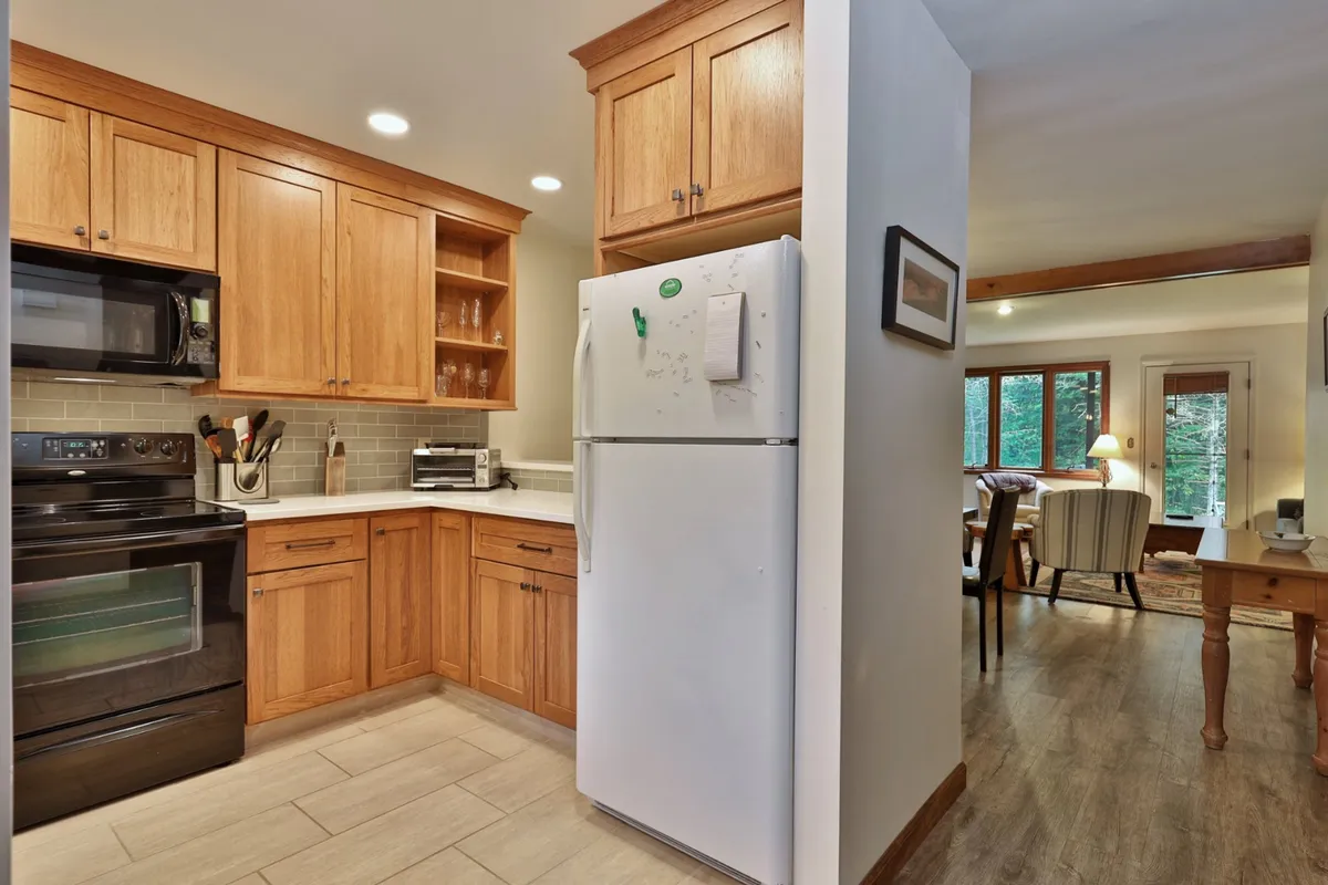 This image features a cozy and functional kitchen with wooden cabinetry, black appliances, and an open layout. The space is clearly designed for cooking, gathering, and entertaining guests, with ample room for preparing meals and sharing memorable moments.